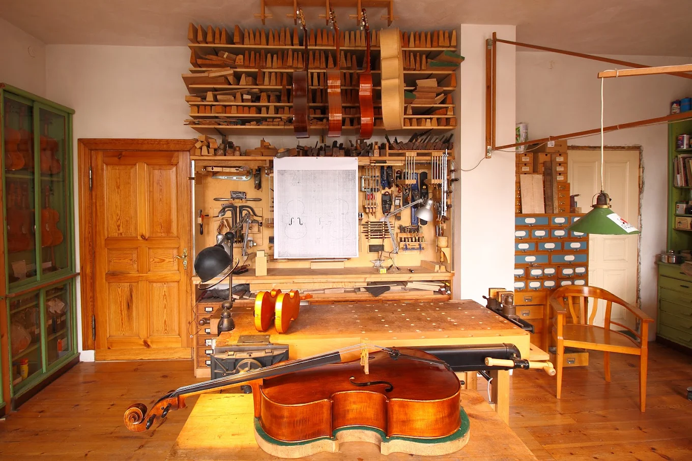 Werkbank mit Cello in Arbeit, Werkzeugwand und Konstruktionszeichnung